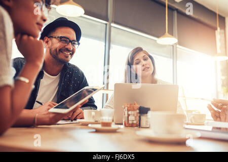 Portrait de jeune homme assis et en parlant avec des amis dans un café. Jeunes à un café avec tablette numérique et la Banque D'Images