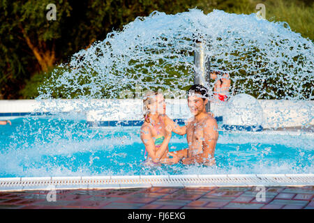 Couple in swimmning piscine sous fontaine éclaboussante. La chaleur de l'été. Banque D'Images