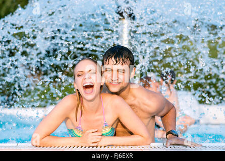 Couple in swimmning piscine sous fontaine éclaboussante. La chaleur de l'été. Banque D'Images