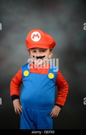 Garçon habillé en Super Mario Bros contre fond gris. Banque D'Images