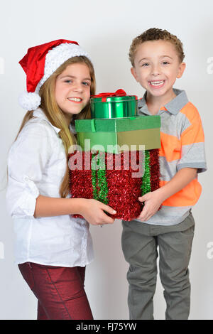 Jeune fille et garçon tenant des cadeaux de Noël et s'amuser tout en se posant contre - fond blanc. Banque D'Images