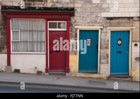 Trois portes avant (1 rouge, 2 bleu) côte à côte - elles appartiennent à de petits chalets sur terrasse pittoresque ancienne Maltongate, Malton, North Yorkshire, Angleterre, Banque D'Images