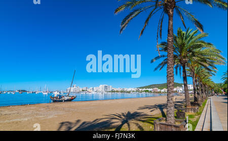 Voilier abandonné sur la plage. Rangées de palmiers bordent la plage, journée ensoleillée au bord de l'eau à Ibiza. Banque D'Images