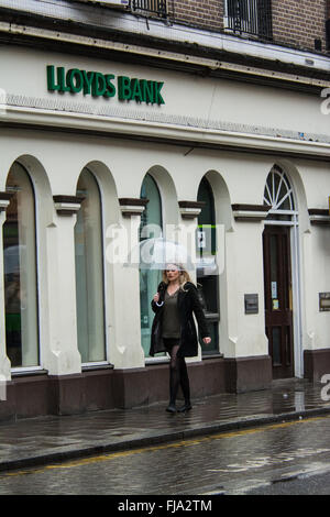 La Banque Lloyds avec blonde femme avec parapluie sous la pluie, Bedford, Bedfordshire Banque D'Images