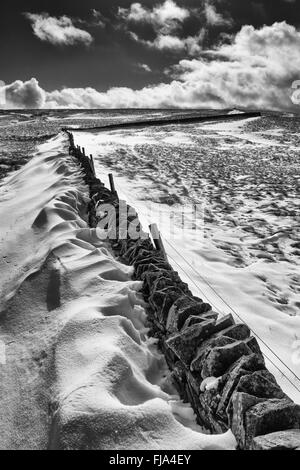 De l'image monochrome a dérivé de la neige sur les côtés d'un mur en pierre sèche qui marque la limite entre le comté de Cumbria et Durham Banque D'Images