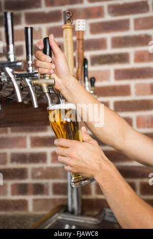 Barman beau versant une pinte de bière Banque D'Images