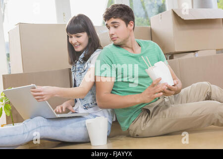 Jeune couple eating noodle and using laptop Banque D'Images