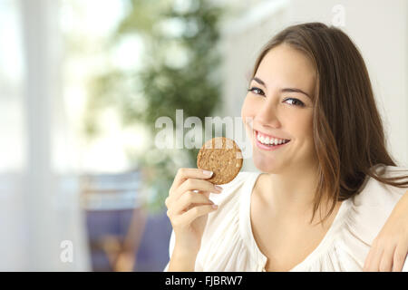 Happy girl montrant un cookie diététiques assis sur un canapé à la maison Banque D'Images