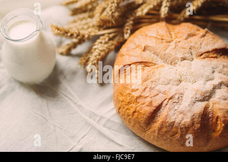 Verseuse en verre avec du lait et du pain sur les textiles blancs Banque D'Images