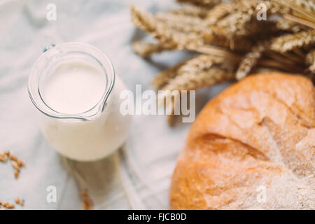 Verseuse en verre avec du lait et du pain sur les textiles blancs Banque D'Images