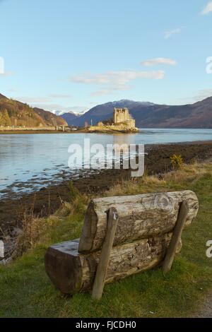 Kyle of Lochalsh, Ecosse - circa Mars 2013 : une vue sur le château d'Eilean Donan avec un banc en bois à l'avant, pris sur une terrasse bien Banque D'Images