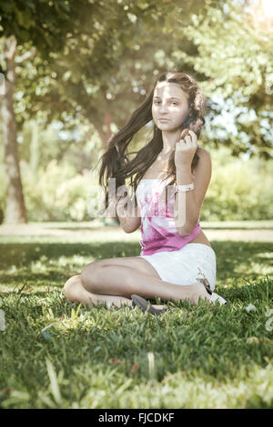 Fille aux cheveux longs assis dans l'herbe verte Banque D'Images