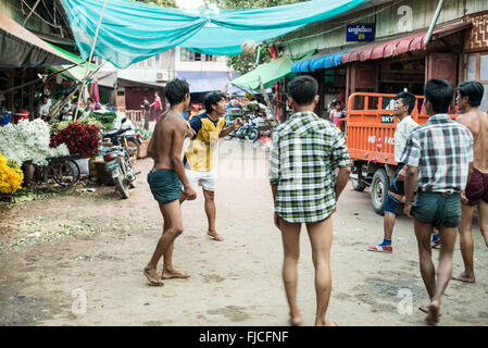 MANDALAY, Myanmar — Un groupe d'hommes birmans jouent au chinlone, également connu sous le nom de caneball, dans une rue de Mandalay. Les joueurs forment un cercle, gardant habilement une boule de rotin tissée en l'air en utilisant diverses parties de leur corps sauf leurs mains. Les spectateurs se rassemblent pour observer les mouvements gracieux et dansants de ce sport traditionnel du Myanmar. Banque D'Images