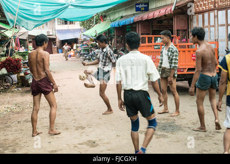 MANDALAY, Myanmar — Un groupe d'hommes birmans jouent au chinlone, également connu sous le nom de caneball, dans une rue de Mandalay. Les joueurs forment un cercle, gardant habilement une boule de rotin tissée en l'air en utilisant diverses parties de leur corps sauf leurs mains. Les spectateurs se rassemblent pour observer les mouvements gracieux et dansants de ce sport traditionnel du Myanmar. Banque D'Images