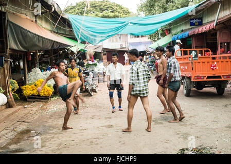 MANDALAY, Myanmar — Un groupe d'hommes birmans jouent au chinlone, également connu sous le nom de caneball, dans une rue de Mandalay. Les joueurs forment un cercle, gardant habilement une boule de rotin tissée en l'air en utilisant diverses parties de leur corps sauf leurs mains. Les spectateurs se rassemblent pour observer les mouvements gracieux et dansants de ce sport traditionnel du Myanmar. Banque D'Images