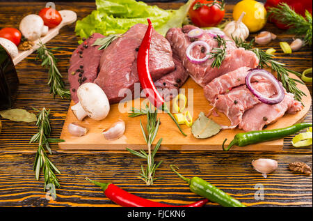 Les poivrons de divers types et de couleur avec de la viande crue sur une planche à découper en morceaux à côté de brins de romarin, salade, tomates, champignons et l'ail. Banque D'Images