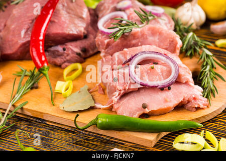 Les poivrons et les oignons de divers types et de couleur avec de la viande crue sur une planche à découper en morceaux à côté de brins de romarin, salade, tomates, champignons et l'ail. Banque D'Images