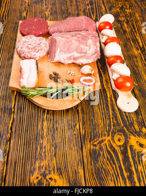 De matières premières sont soigneusement disposées de la viande rouge et la viande de porc sur une planche à découper à côté de poivrons, oignon, branche de romarin, tomates et champignons Banque D'Images