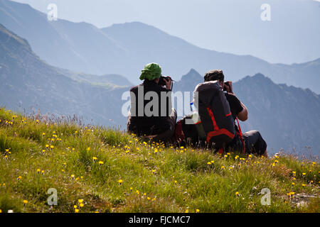 Les randonneurs de couple admiring view et prendre des photos de hautes montagnes Banque D'Images