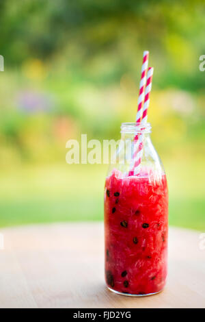 Smoothie pastèque ou de l'eau en bouteille en verre de désintoxication sur table dans jardin avec deux pailles à rayures Banque D'Images