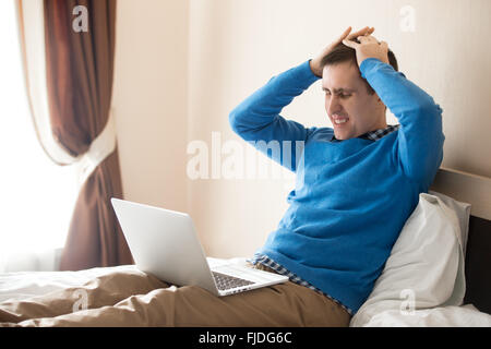 Portrait of young a souligné l'homme assis sur le lit avec coffre portant des vêtements chic et décontracté, tenant sa tête dans les mains Banque D'Images