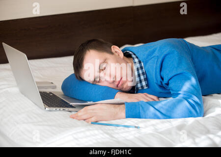 Portrait of attractive young casual man lying on bed, dormir en face de l'ordinateur portable, endormi, fatigué, surmené ou paresseux Banque D'Images