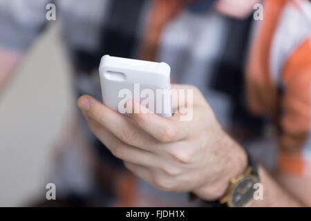 Young man holding white téléphone mobile en main, la messagerie instantanée, à l'aide d'application pour smartphone, close-up Banque D'Images