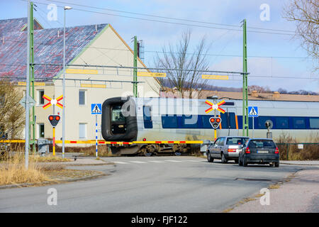 Solvesborg, Suède - 27 Février 2016 : Les voitures sont arrêtés à un passage à niveau alors que le train passe. Les feux rouges clignotent. Banque D'Images