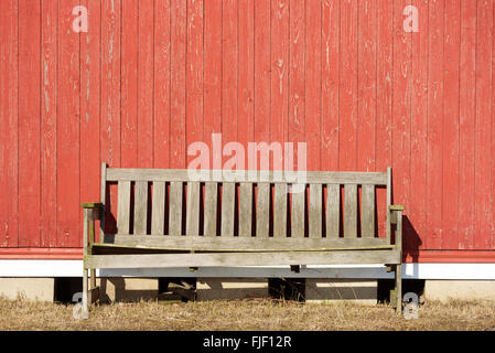 Un vieux banc non peinte sur un mur en bois rouge. Soleil brille à l'extérieur vide de meubles. L'espace de copie sur mur. Banque D'Images