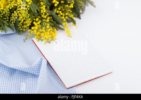Bouquet de mimosa jaune, bleu serviette et bloc-notes sur fond blanc Banque D'Images