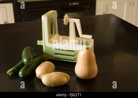 Un brillant nouveau spiralizer assis sur une surface de travail de cuisine intérieure à côté de courgettes, pommes de terre et de courge Butternut. Banque D'Images