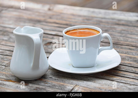 L'un blanc tasse pleine de café expresso avec brown crema sur porcelaine soucoupe sur petit pot à lait sur old vintage en bois bambou tabl Banque D'Images