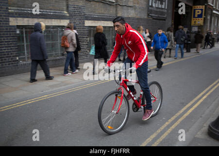 Jeune homme asiatique avec un vélo rouge et red Tracksuit top vélo sur Brick Lane dans l'Est de Londres, au Royaume-Uni. Ce secteur est particulièrement connu pour les Indiens, c'est la cuisine asiatique. Aujourd'hui, c'est le cœur de la communauté bangladaise de Londres et est connu pour certains comme Banglatown. Banque D'Images