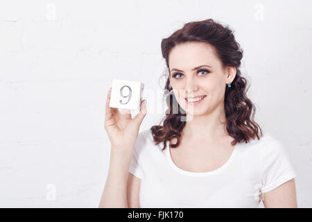 Young girl smiling and holding a numéro neuf. Fille vêtue d'un t-shirt blanc. L'expression émotionnelle. Banque D'Images