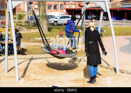 Solvesborg, Suède - 27 Février 2016 : deux enfants dans une grande balançoire à une aire de jeux, avec une femme debout à côté. Rea Banque D'Images
