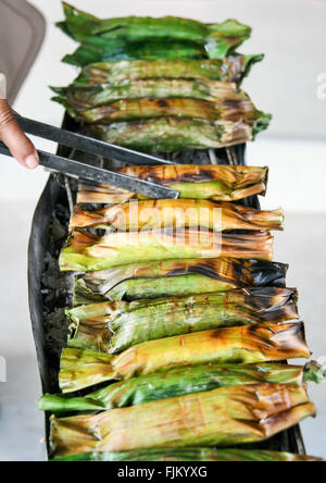 Cuisson du riz collant femme enveloppée dans des feuilles de bananier sur un étal de marché à Khao Sok, Thaïlande Banque D'Images