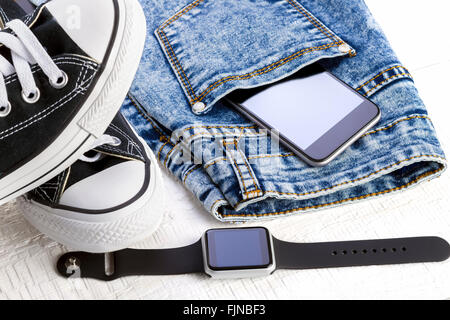 Smartphone, smartwatch, jeans et chaussures de sport blanc sur les planches de bois. Banque D'Images