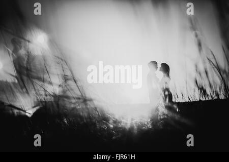 Photographie noir blanc silhouette romantique et couple kissing on meadow background sunset Banque D'Images