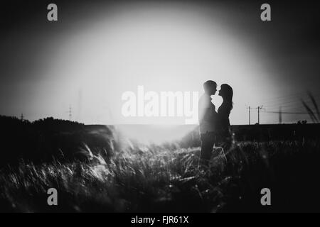 Photographie noir blanc silhouette romantique et couple kissing on meadow background sunset Banque D'Images