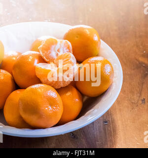 Mandarines, Citrus reticulata, avec un pelé dans un bol blanc. Banque D'Images