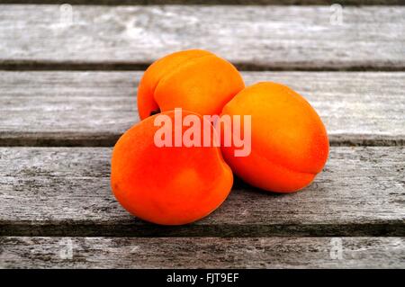 Trois abricots mûrs orange vif sur une table en bois Banque D'Images