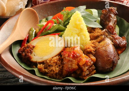 Nasi Kuning, Javanais curcuma riz avec variété de plats ; plaquée sur la vaisselle en terre cuite. Banque D'Images