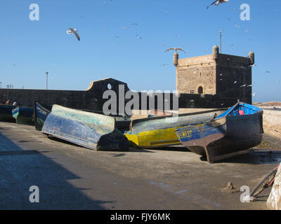 Bateaux de pêche jaune et bleu se trouvant sur leurs côtés à Essaouira au Maroc avec l'ancien fort portugais dans l'arrière-plan. Banque D'Images