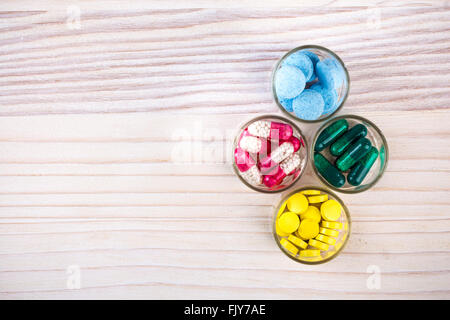 Divers comprimés et gélules dans des contenants en verre sur la table en bois clair Banque D'Images