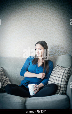 Jeune femme se reposant sur un canapé-lit avec tasse de thé Banque D'Images