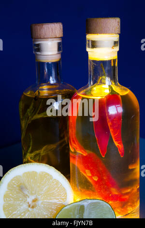 Une paire de bouteilles en verre transparent rempli d'huile d'olive et assaisonné avec des herbes et épices, en particulier le romarin, piment, curcuma, Banque D'Images