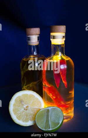 Une paire de bouteilles en verre transparent rempli d'huile d'olive et assaisonné avec des herbes et épices, en particulier le romarin, piment, curcuma, Banque D'Images