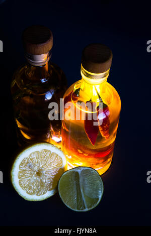 Une paire de bouteilles en verre transparent rempli d'huile d'olive et assaisonné avec des herbes et épices, en particulier le romarin, piment, curcuma, Banque D'Images