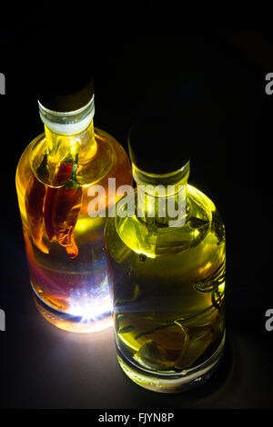 Une paire de bouteilles en verre transparent rempli d'huile d'olive et assaisonné avec des herbes et épices, en particulier le romarin, piment, curcuma, Banque D'Images