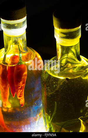 Une paire de bouteilles en verre transparent rempli d'huile d'olive et assaisonné avec des herbes et épices, en particulier le romarin, piment, curcuma, Banque D'Images